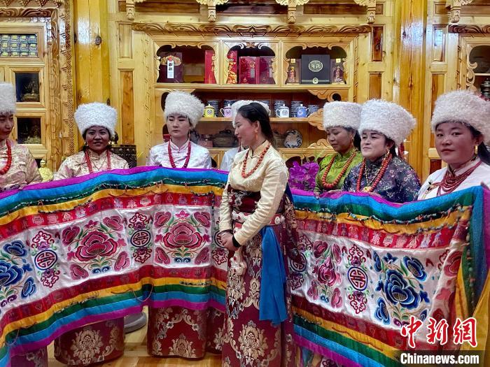 圖為女性展示村民自發(fā)繡制的“百米五彩哈達(dá)”?！±钣穹?攝